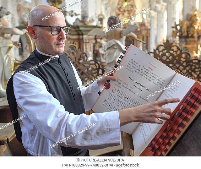 29 August 2018, Neuzelle, Germany: Cistercian monk Father Kilian Mueller looks into a book with prayer texts in the choir stalls of the Catholic church of the...