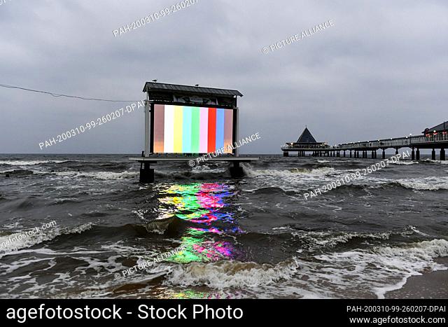 06 March 2020, Mecklenburg-Western Pomerania, Heringsdorf: The light of an LED video wall is reflected in the water of the Baltic Sea at the pier in the evening...