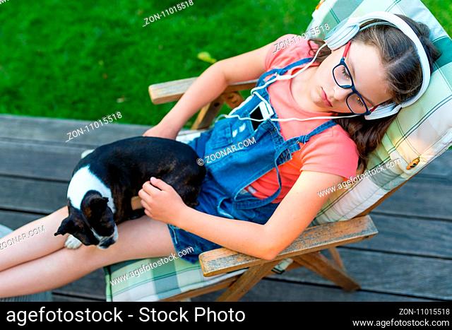 Girl resting in the garden with her dog and listening to music - sweet boston terrier puppy on her legs