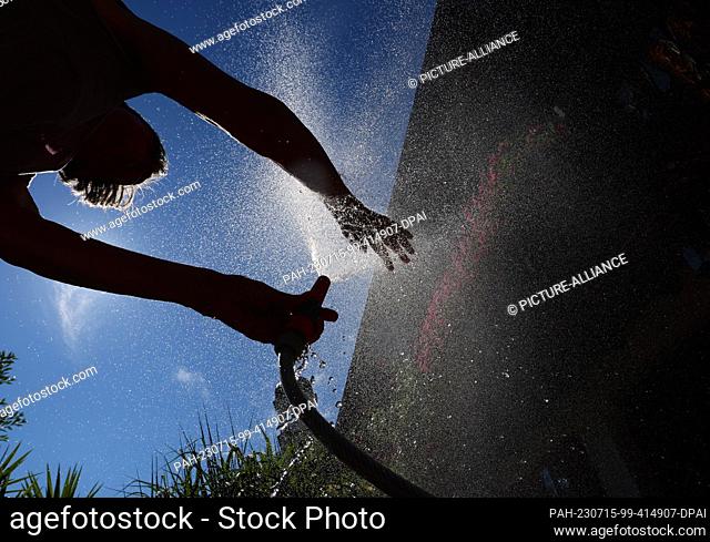 15 July 2023, Bavaria, Kaufbeuren: A woman cools off in a garden with water from a garden hose. Photo: Karl-Josef Hildenbrand/dpa