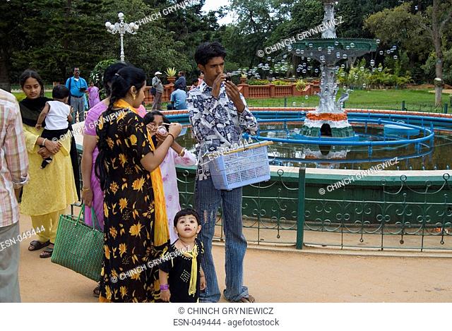 Street trader selling soap bubbles to Indian day trippers in city park - Lalbagh Botanical Garden, Bangalore, Karnataka India