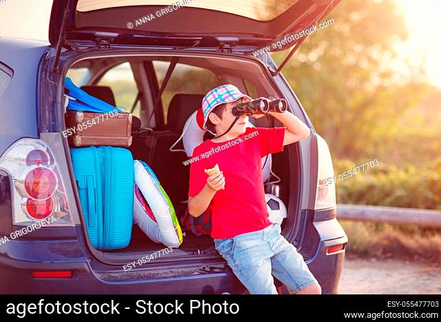 Boy resting in nature at sunset. child sitting in car filled with traveling accessories