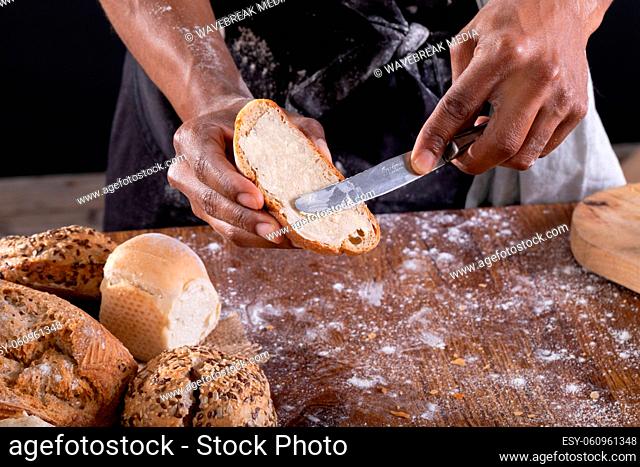 Midsection of african american male baker applying butter on bread slice