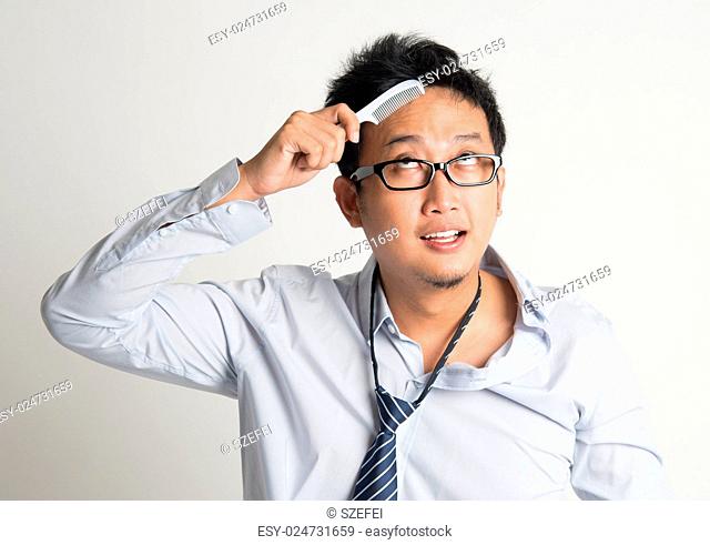 Asian businessman combing hair in morning in hurry, on plain background