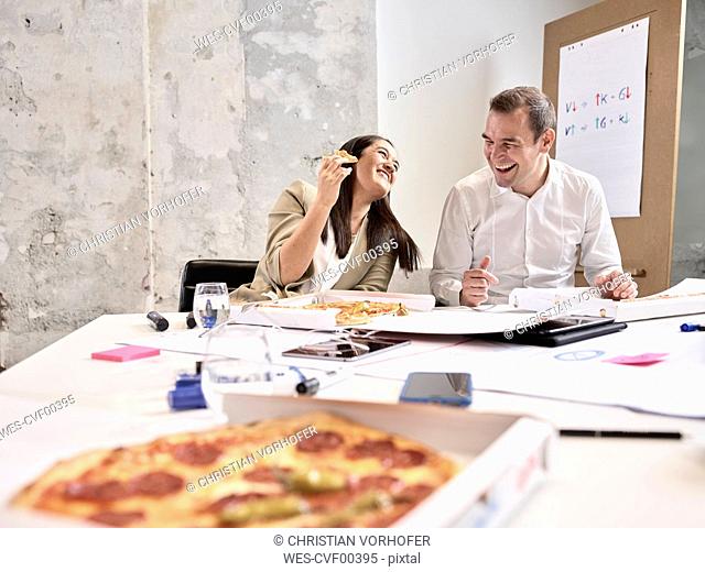 Laughing colleagues having lunch break with pizza in conference room