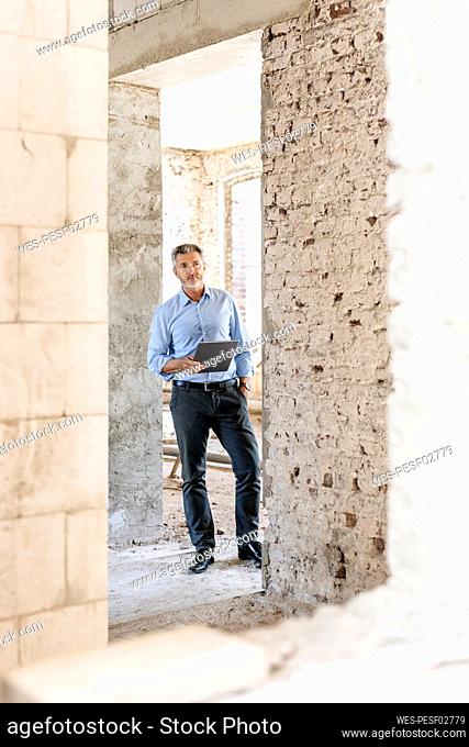 Male architect with hand in pocket holding digital tablet at construction site