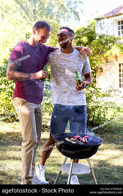 Young men with beer bottles standing near barbecue grill