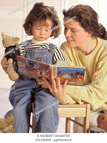 mother with long brown plait reads at a picture book resting on a kid s chair with her daughter, 4 years, holding her teddy in her arm  - GERMANY, 27/04/2003