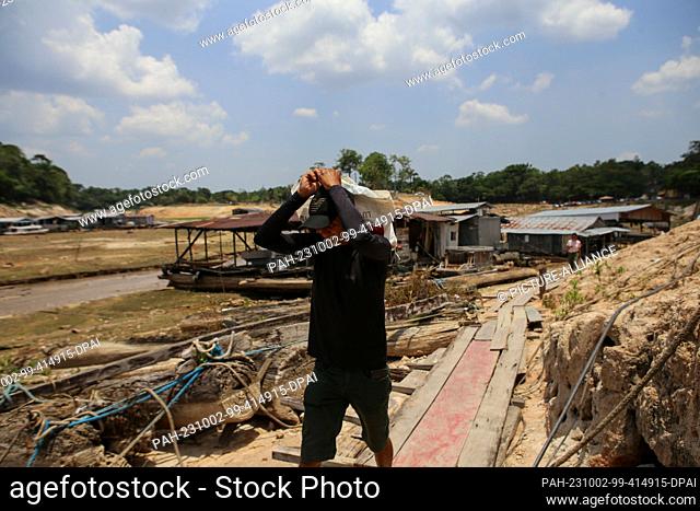 30 September 2023, Brazil, Manaus: A man carries a bag as he walks through the floating houses in Marina do Davi, west of Manaus