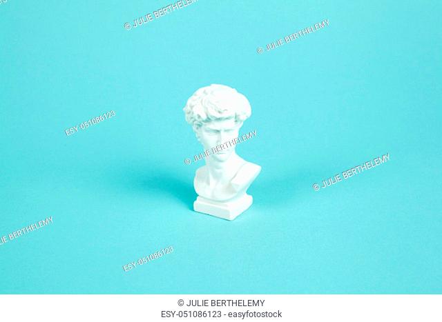 a white resin bust of David on a turquoise background. Summer atmosphere. Minimal color still life photography
