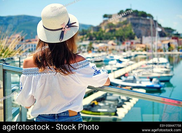 Rear back view pretty woman wear straw hat pose outdoor look at Denia castle marina scenery, travel at historical coastal city in province of Alicante, Spain