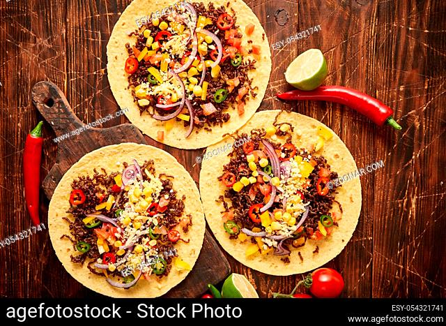 Healthy corn tortillas with grilled beef, fresh hot peppers, cheese, tomatoes over rusty wooden table background, top view, copy space