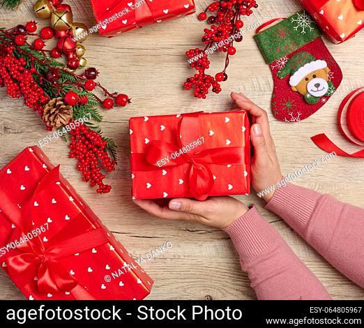 Woman is packing gifts, the pre-holiday bustle and preparations for Christmas. Gifts wrapped in red paper and tied with ribbon