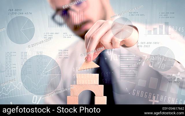 Young handsome businessman using wooden building blocks with data and numbers around him