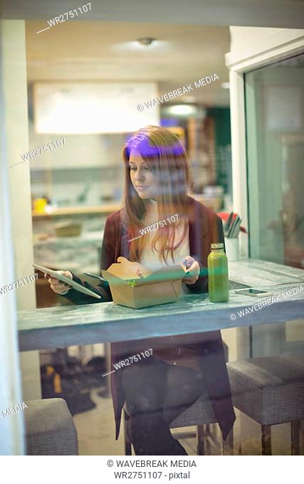 Woman using digital tablet while eating salad