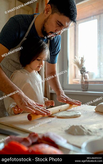 Boy with father rolling pizza dough in kitchen