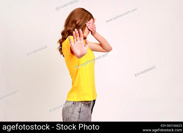 I'm not watching. Profile portrait of scared shamed teenager girl in casual yellow T-shirt covering eyes and showing stop gesture, hiding eyesight