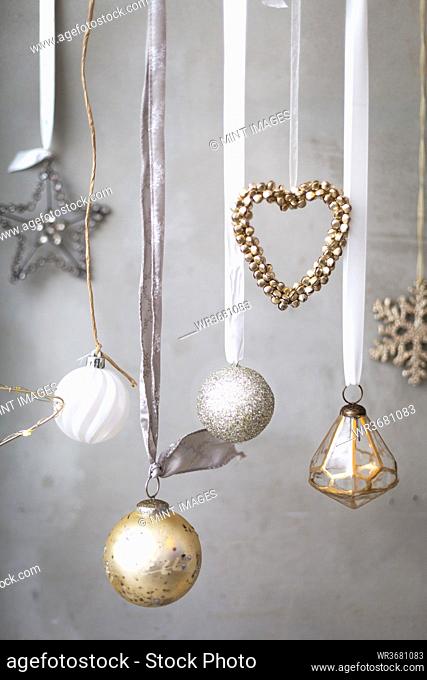 Christmas decorations, silver, white and gold baubles on ribbons on grey background