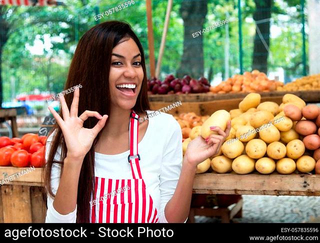 Latin american saleswoman at farmers market presenting potato and vegetables and other healthy food