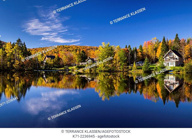 Cottages and fall foliage color in the trees reflected in a calm lake at La Beauport, Quebec, Canada