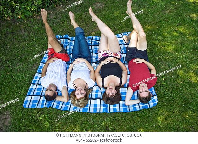 Four young people lying on a blanket in the garden, smiling