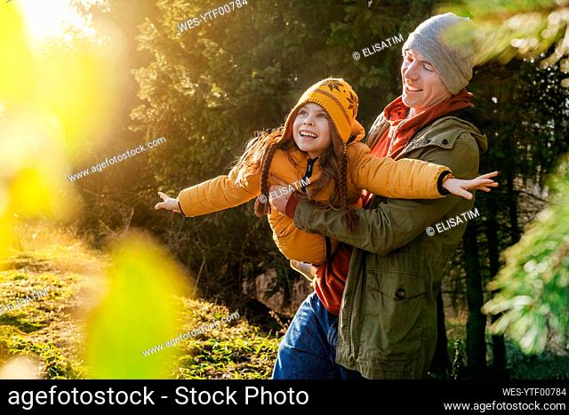 Father carrying playful daughter in forest