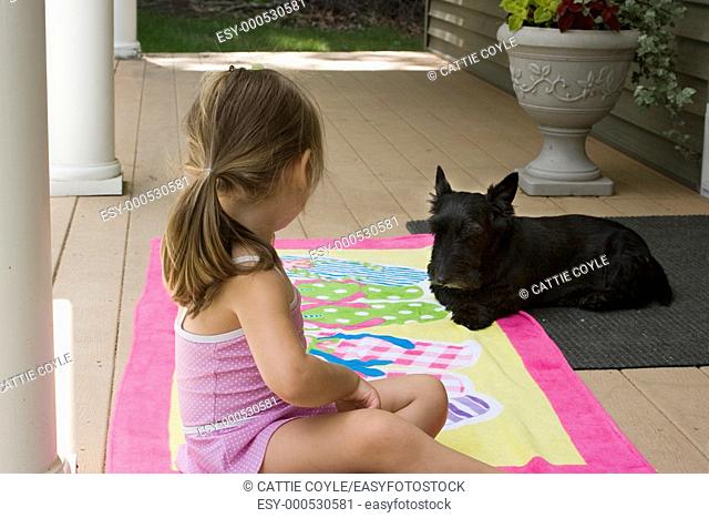 4-year old girl enjoying a summer afternoon on the front porch with her dog friend, a Scottish Terrier