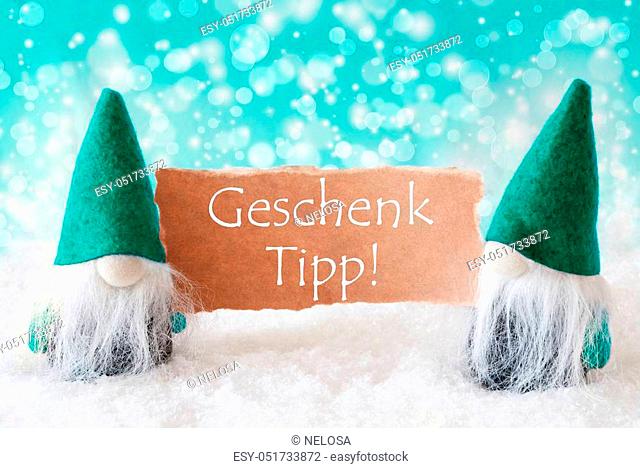 German Text Geschenk Tipp Means Gift Tip. Christmas Greeting Card With Two Turqoise Gnomes. Sparkling Bokeh Background With Snow