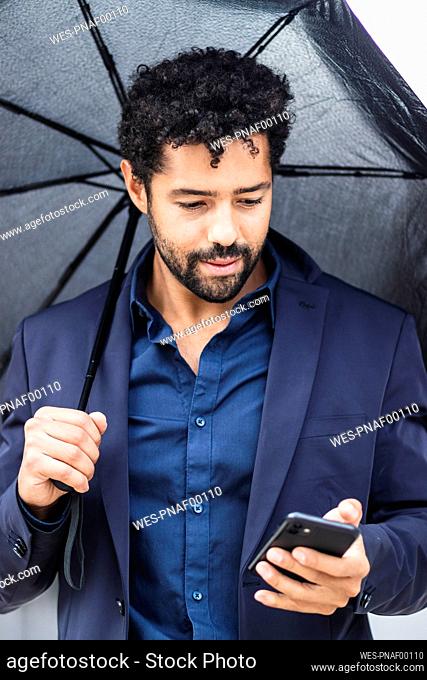Entrepreneur with umbrella using smart phone in city