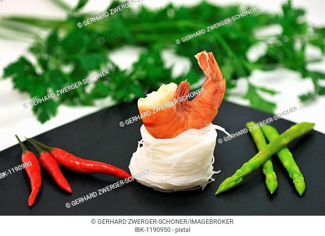 Scampi on a bed of rice noodles with Thai asparagus and red chilli in front of parsley