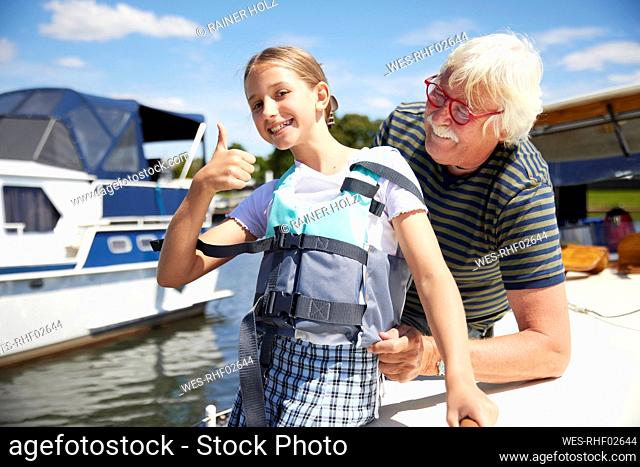 Smiling girl gesturing thumbs up by grandfather on boat deck