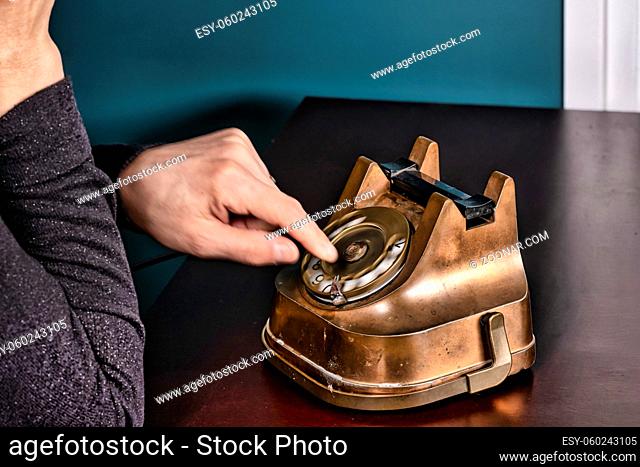 Retro antique classic outdated copper with black color rotary telephone from circa 1950s on wooden table, green wall background