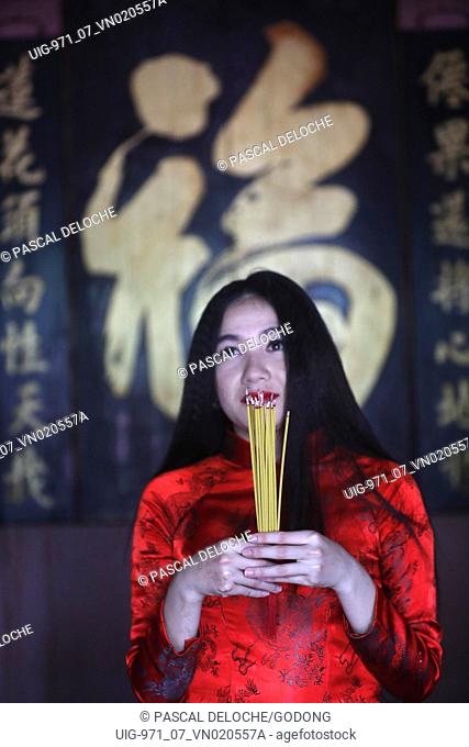 The Jade Emperor Pagoda. Vietnamese woman in red traditional long dress Ao Dai praying with incense sticks. Ho Chi Minh City. Vietnam