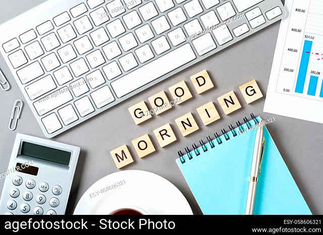 Good morning message with letters on wooden cubes. Still life of workspace with supplies. Flat lay grey surface with computer keyboard and spiral notebook