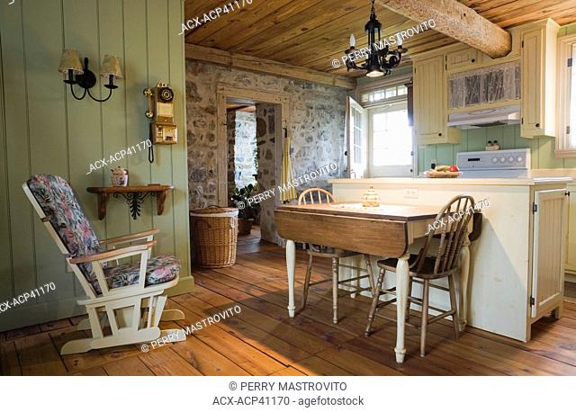 Antique table, chairs and furnishings in the kitchen of an Old Canadiana 1722 cottage style fieldstone and wooden siding Residential Home, Quebec, Canada