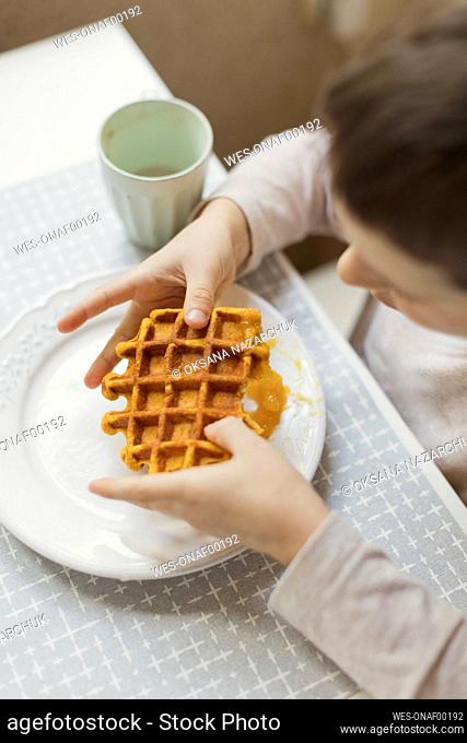 Boy holding waffle on dining table in kitchen