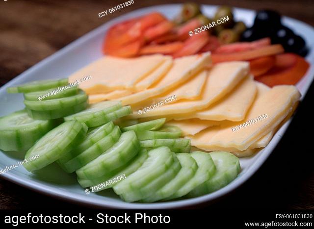 Closeup of plate with cheese and vegetables isolated on the wooden table background