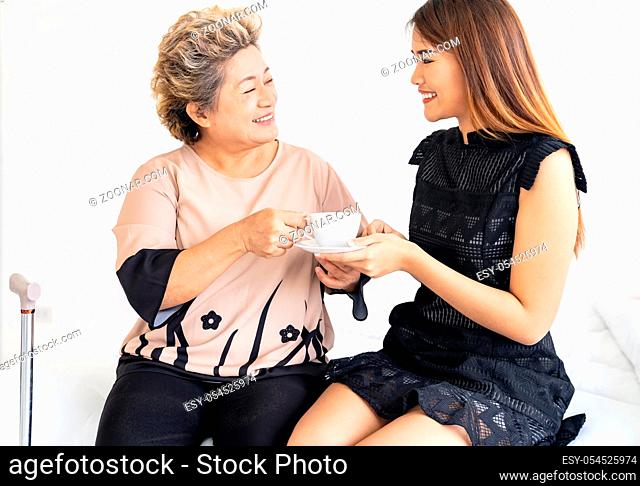Caregiver woman giving coffee to old elderly woman on the bed and check up her at home