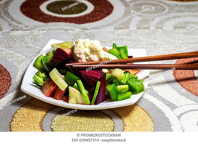 Chopsticks and green salad. Salad is of simple vegetables