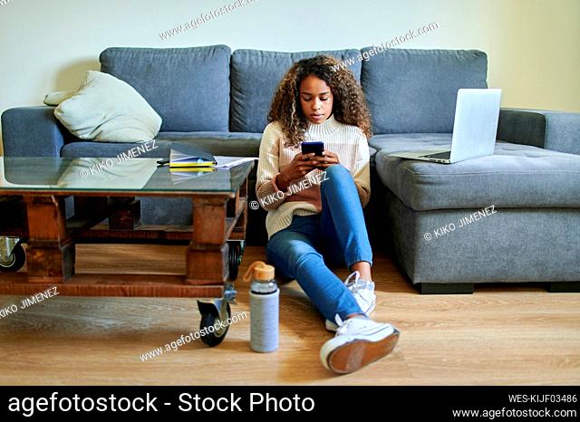 Young woman using mobile phone while sitting on floor in living room at home