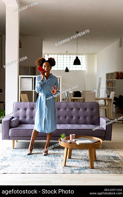 Young woman talking on speaker of smart phone in living room at home