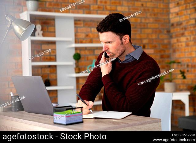 Man talking on smartphone and taking notes while sitting on his desk