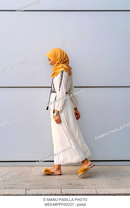 Young muslim woman wearing yellow hijab and walking in front of a white wall