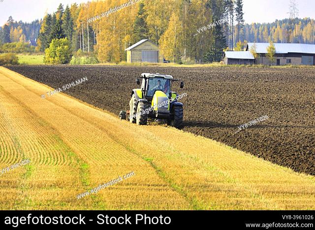 Farmer plowing field with green Valtra tractor and plough on a sunny autumn afternoon in South of Finland. Jokioinen, Finland. October 2, 2020
