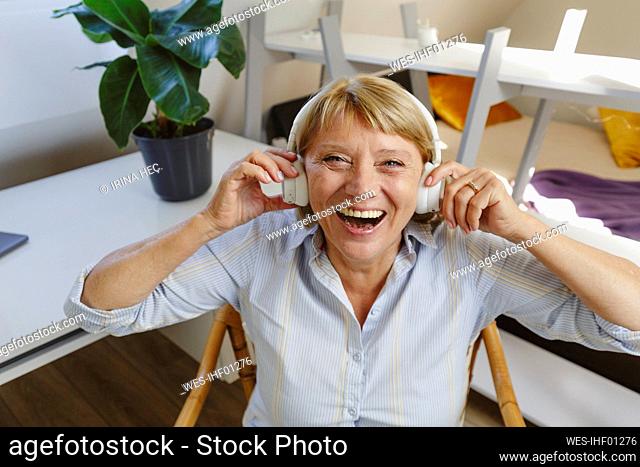 Cheerful senior woman listening music through wireless headphones
