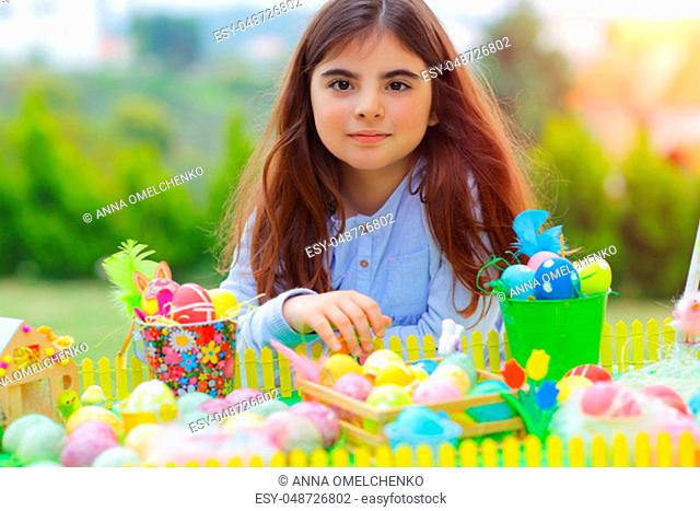Portrait of a cute little girl enjoying Easter holiday, having fun outdoors and playing with many different colorful eggs, traditional Easter symbol