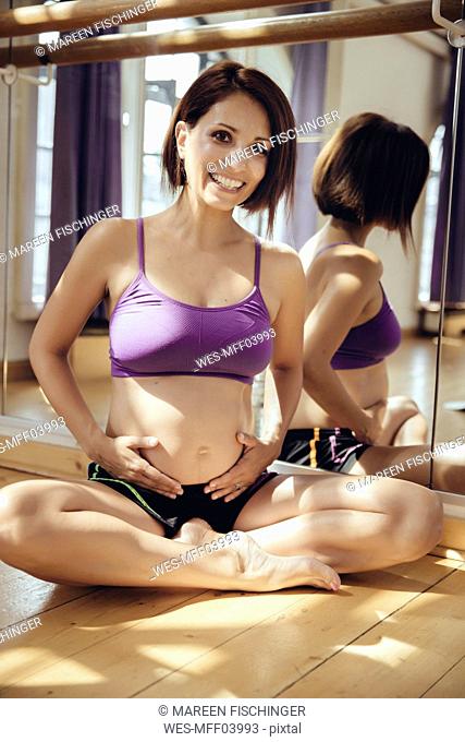 Portrait of smiling sporty pregnant woman sitting on floor in exercise room