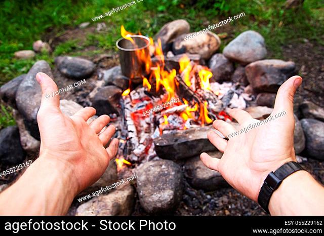 Men's hands are warming around the campfire in the forest