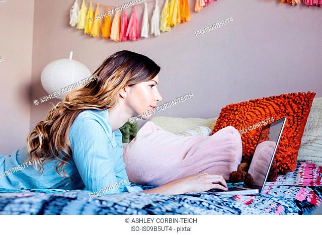 Young woman lying on shabby chic bed looking at laptop