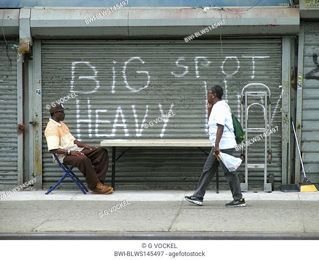 man sitting in front of shutters of a closed shop at 125th street in Harlem, USA, Manhattan, Harlem, New York